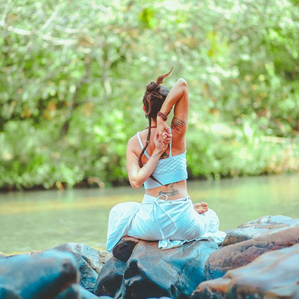 Person meditating peacefully outdoors near water.